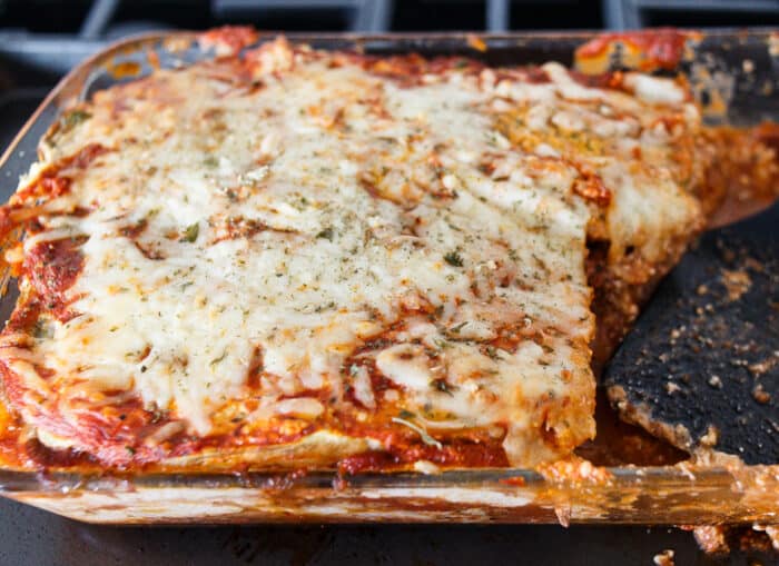 A clear casserole dish filled with eggplant lasagna with melted cheese on top. One piece of lasagna is missing.