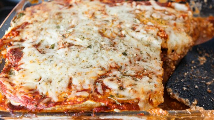 A clear casserole dish filled with eggplant lasagna with melted cheese on top. One piece of lasagna is missing.