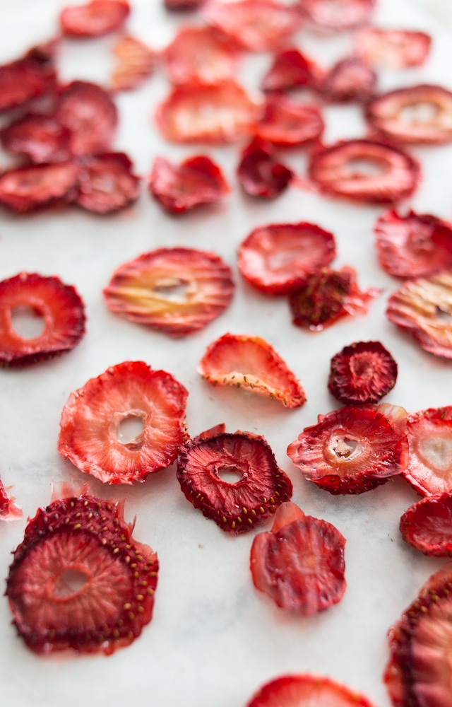 Several oven dried strawberries - still bright red but thinner than an average slice of strawberry - sitting on a white counter.