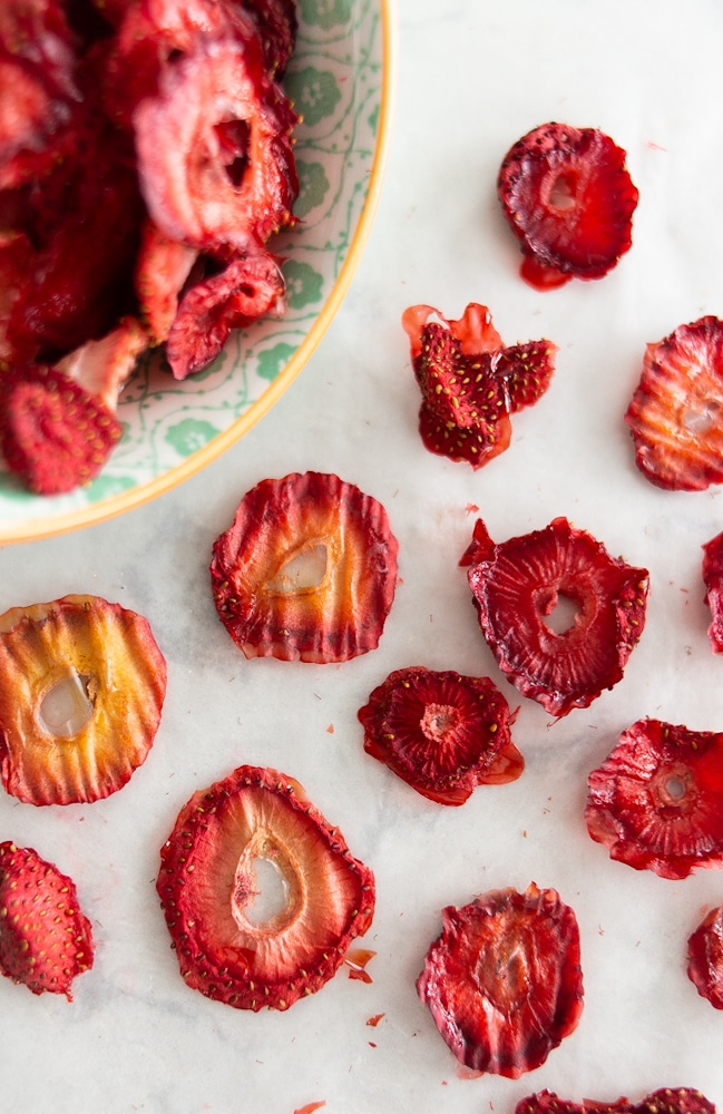 A bowl of oven dried strawberries tipped over with several strawberries sitting on a white counter.