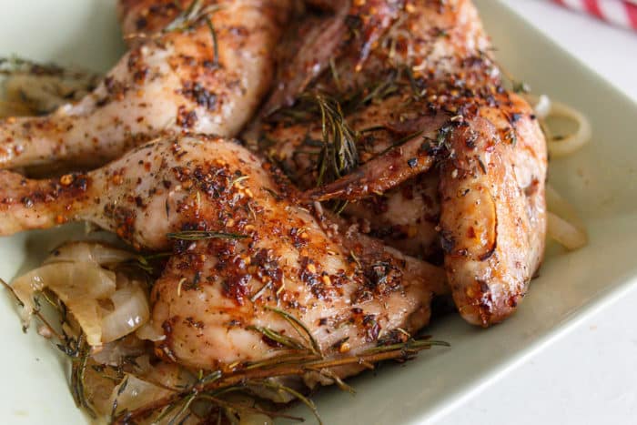 A chicken with both breasts and legs out to each side, cooked and topped with rosemary and thyme.