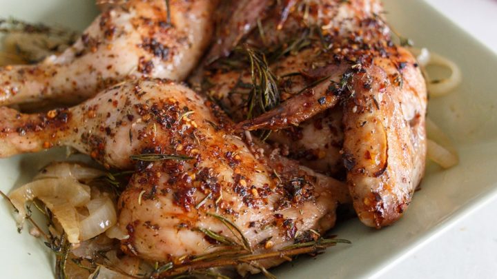 A chicken with both breasts and legs out to each side, cooked and topped with rosemary and thyme.